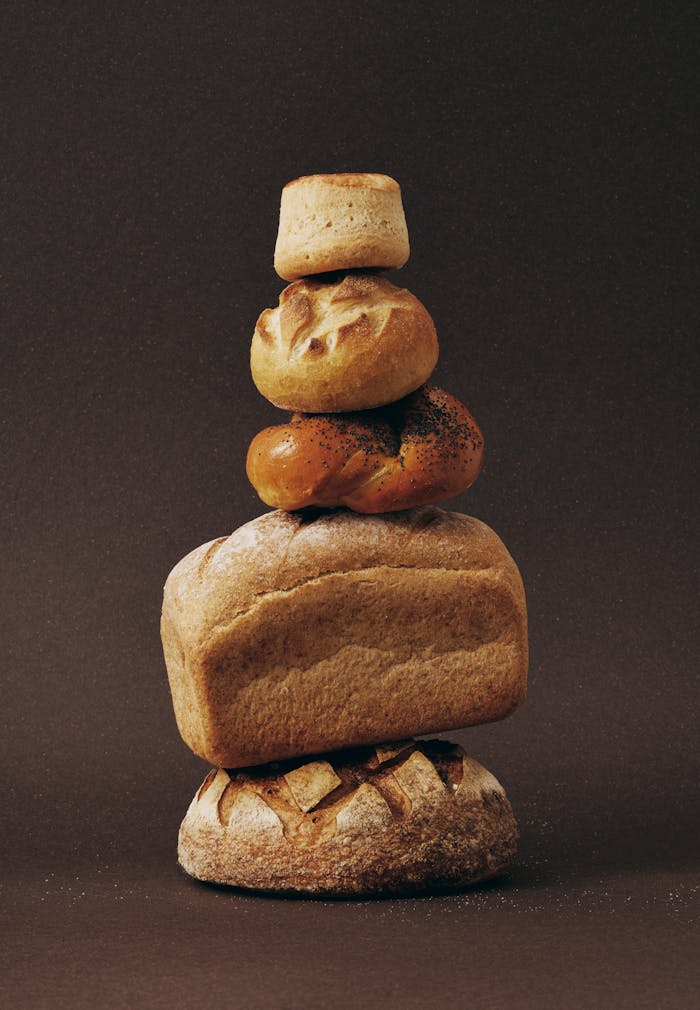 Home Stack of various bread loaves artfully arranged against a dark background.