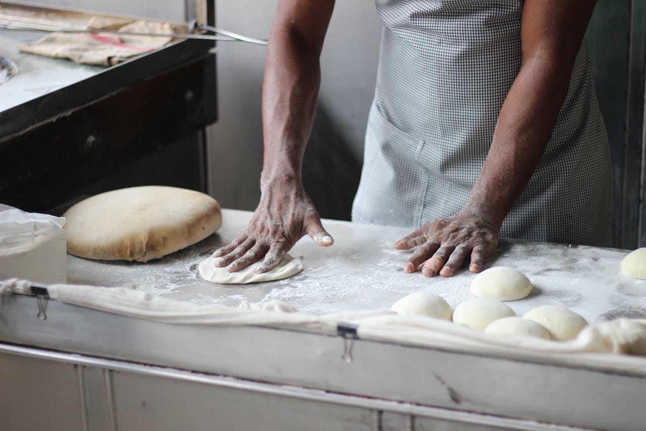 Home A baker in an indoor kitchen kneading dough for bread preparation, showcasing traditional baking techniques.