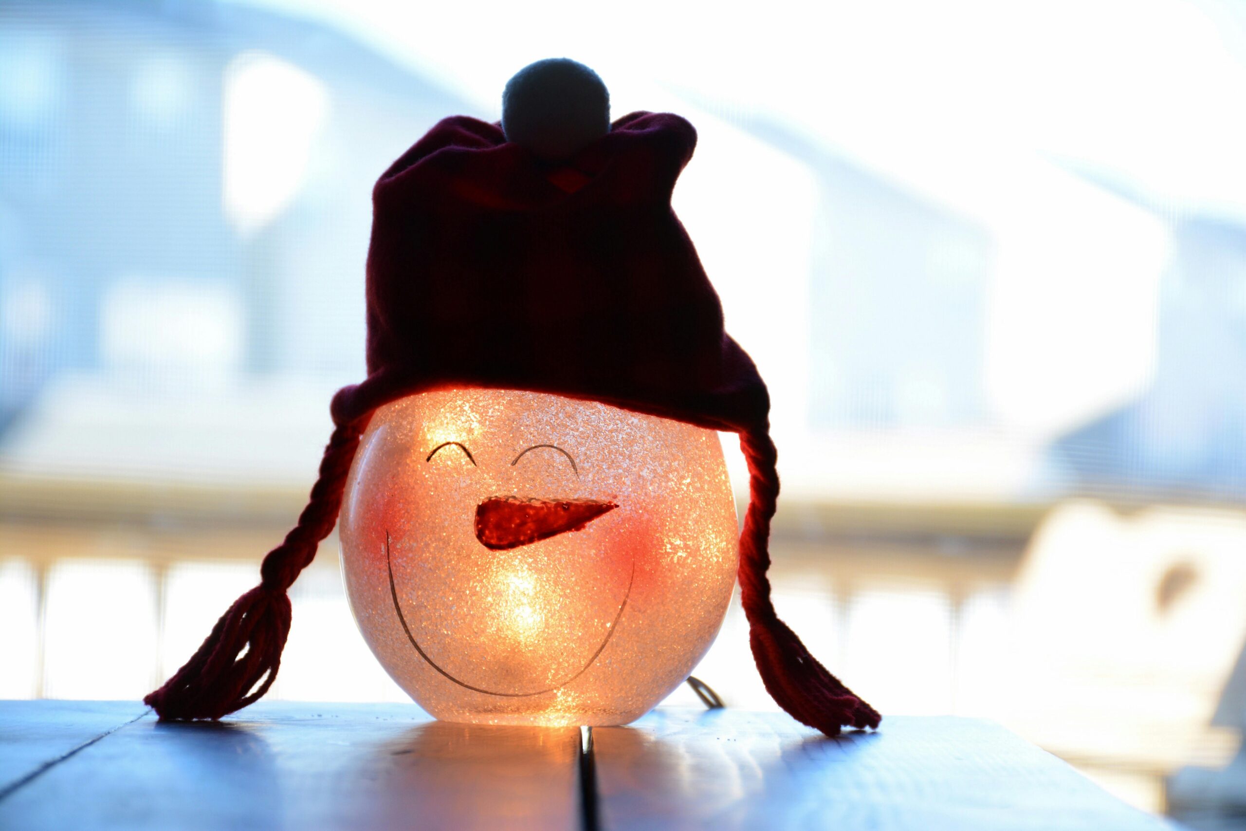 Charming snowman decoration with knitted hat glowing warmly indoors on a wooden table.